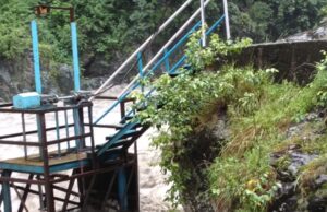 निरंतर हो रही भारी बारिश से मंडी शहर के लिए पेयजल आपूर्ति बाधित, जल शक्ति विभाग ने की सहयोग की अपील A strong flow of water rushing through a metal water control structure with a staircase, surrounded by greenery and rocks.